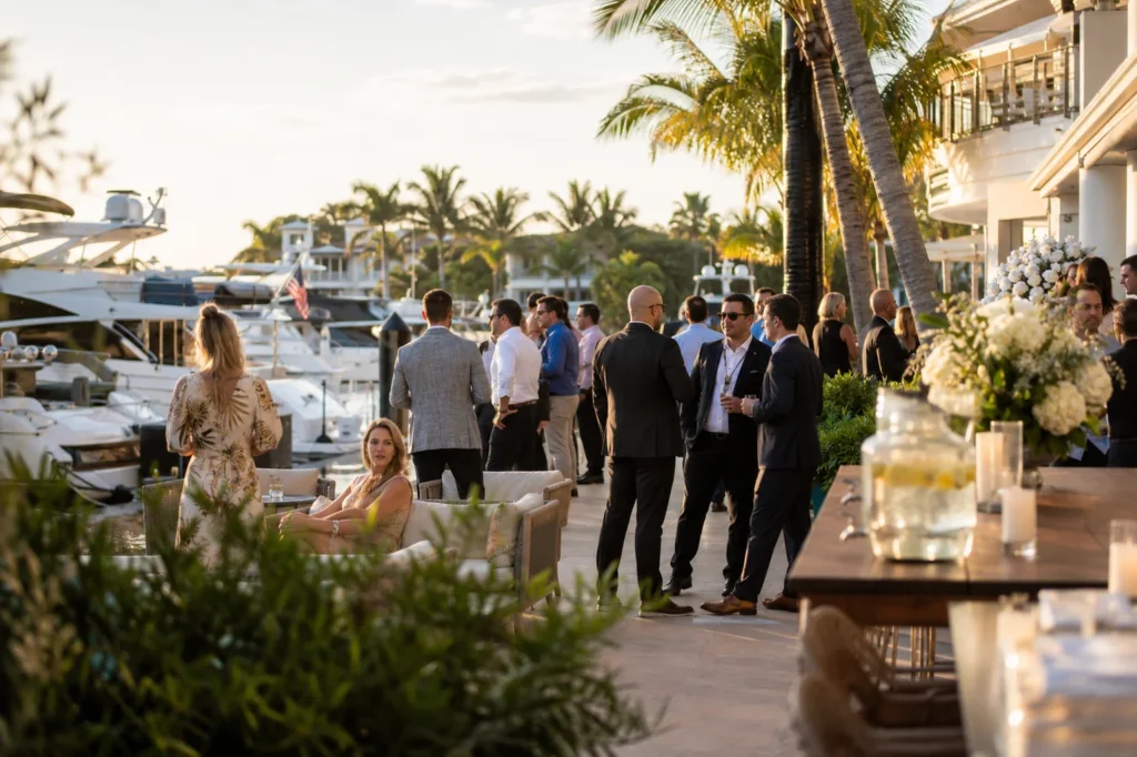 This image is showing an elegant Fort Lauderdale waterfront event venue with luxury yachts, palm trees, and a sophisticated coastal entertainment atmosphere during golden hour.
